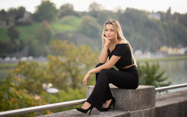 A blonde woman with long hair and a warm smile sits wearing black high heels and an off-shoulder outfit, captured in sharp 4K Ultra HD with a soft depth of field background.