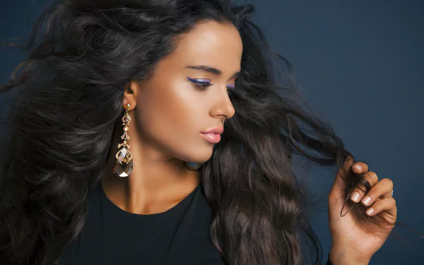Wind-swept dark-haired woman model in profile wearing dangling earrings, glossy skin and flowing hair — 5K Ultra HD PC desktop wallpaper/background.