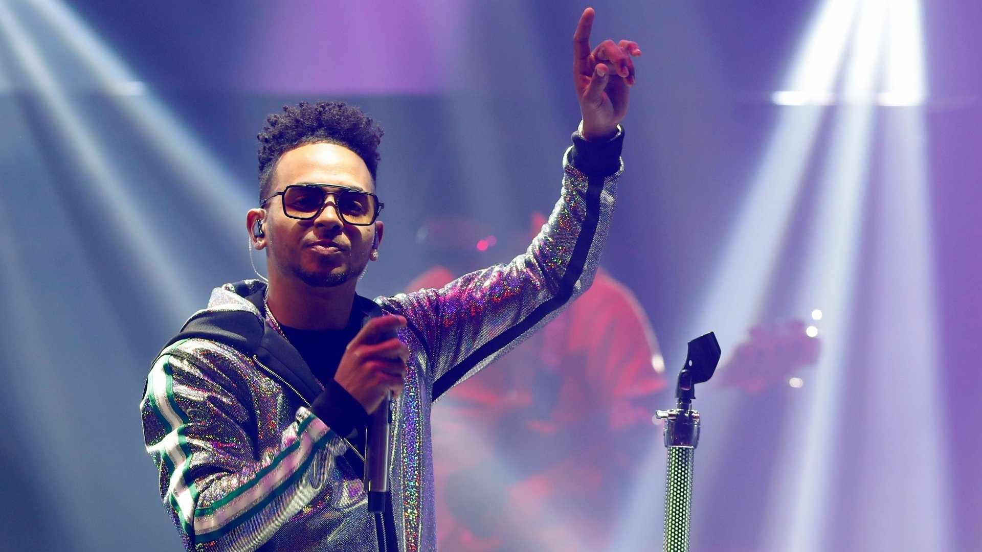 Ozuna on stage in a sequined jacket, pointing upwards, in an HD wallpaper and background.