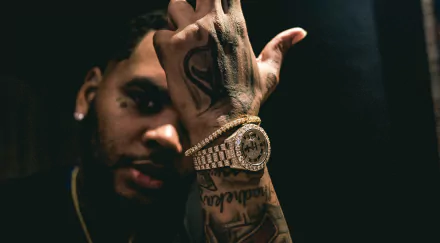 HD wallpaper featuring an individual posing with a hand over the face, showcasing elaborate tattoos and a luxurious watch.
