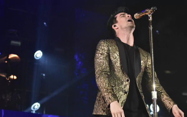 HD wallpaper of a Panic! at the Disco performance with the lead singer on stage in a golden jacket, singing into a microphone.