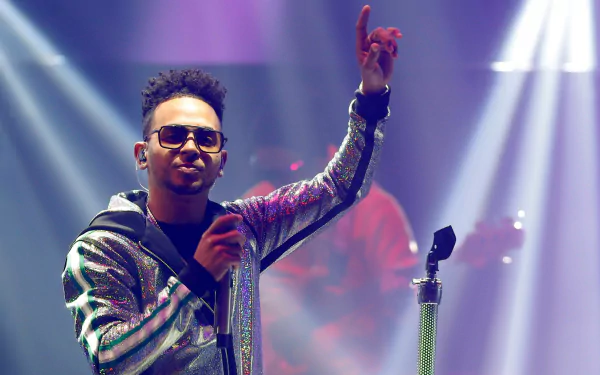 Ozuna on stage in a sequined jacket, pointing upwards, in an HD wallpaper and background.